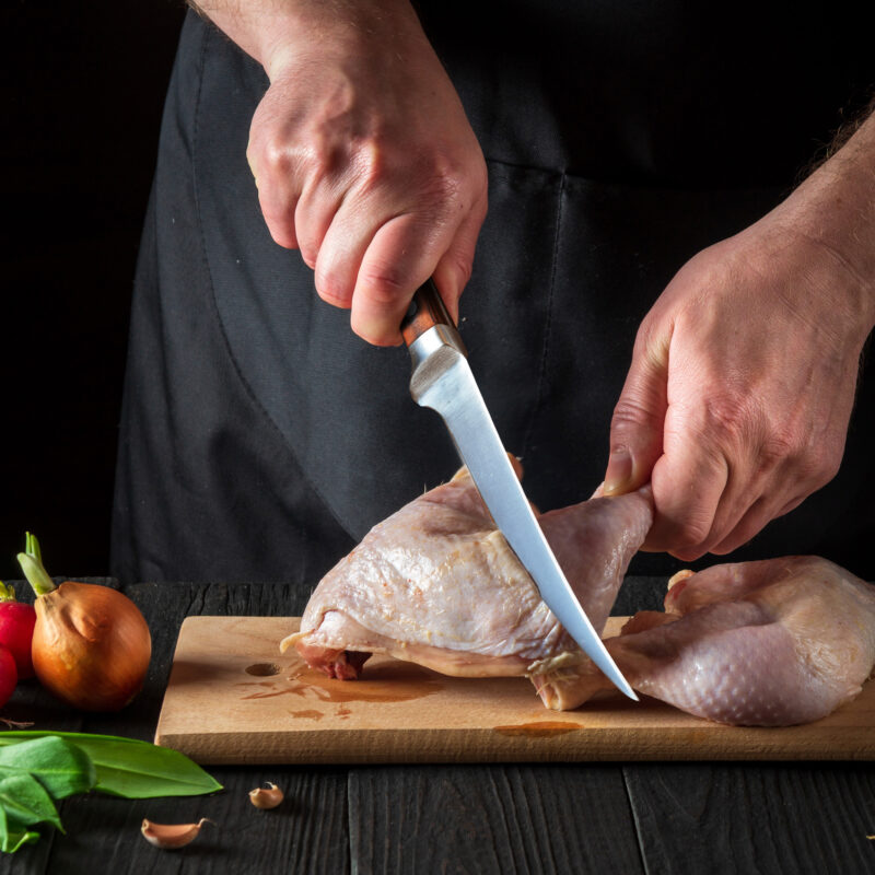 man cutting chicken thigh with sharp fillet knife