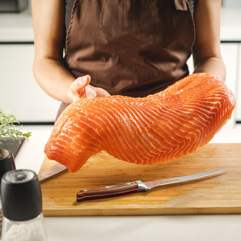 woman holding large salmon fillet over cutting board