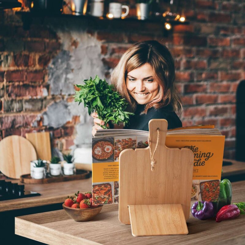 young woman in a cosy kitchen looking at recipe book which rests on cookbook holder